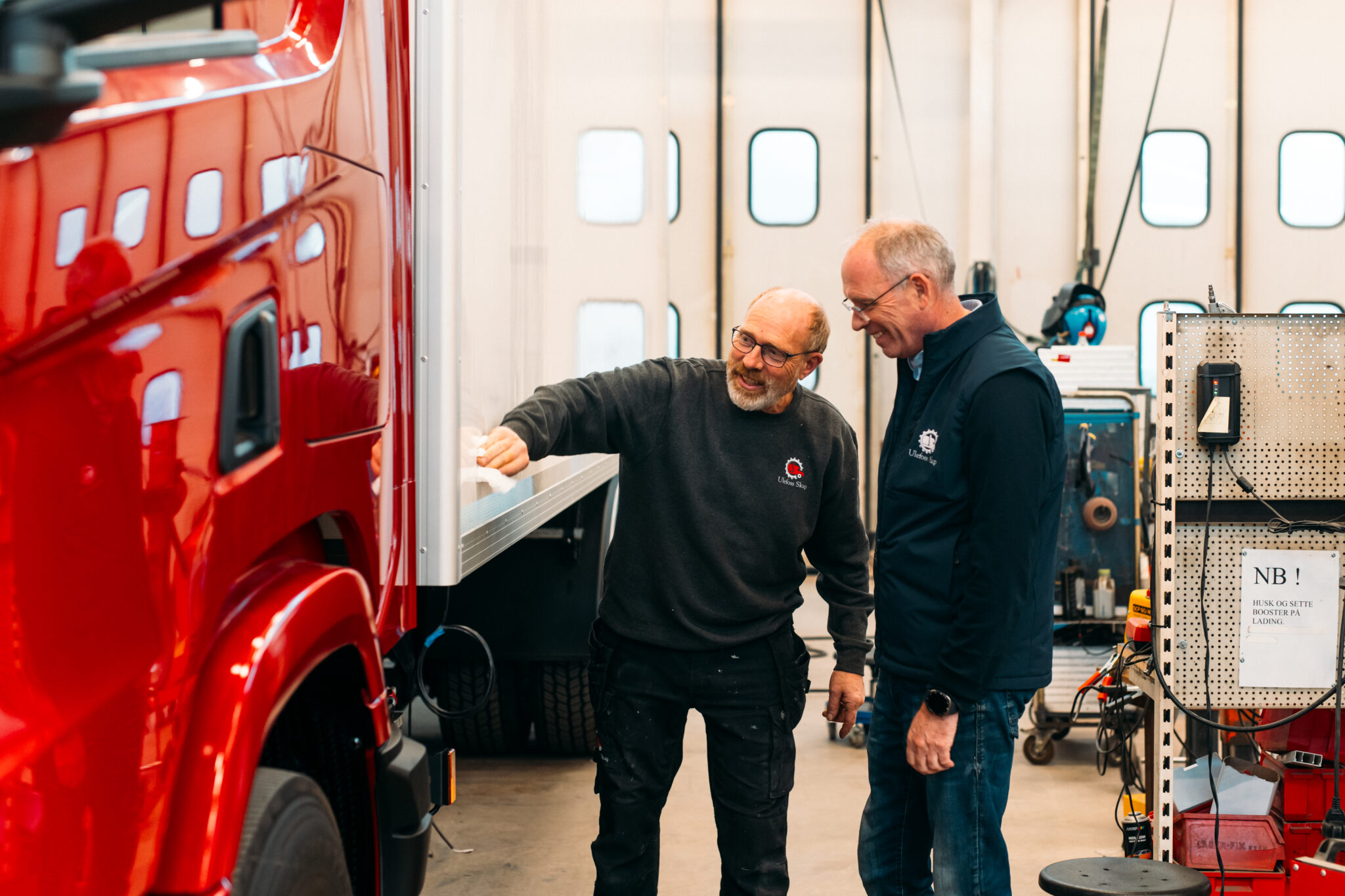To menn smiler og ser på en rød lastebil